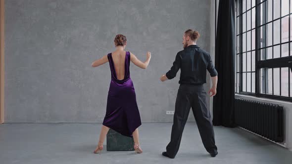 Man Teaching Woman Dancing Tango in Grey Studio Against Large Windows