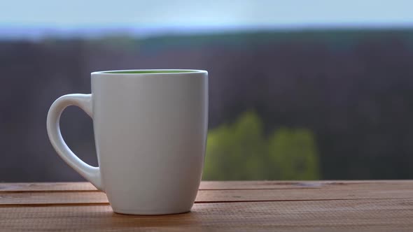 Cup of Hot Tea or Coffee Stands By an Open Window and Emits Steam