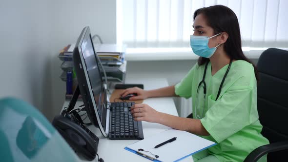 Concentrated Professional Doctor Surfing Internet on Computer Sitting at Table Indoors