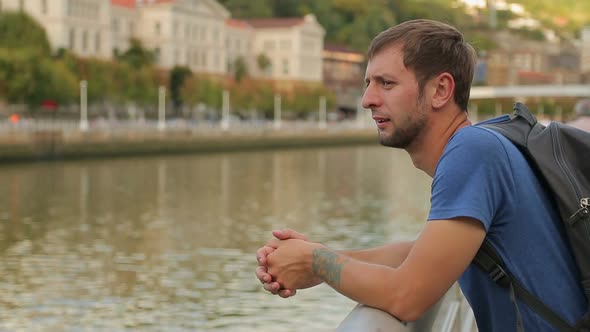 Happy Young Man Enjoying View by the Riverside, Looking at City Architecture