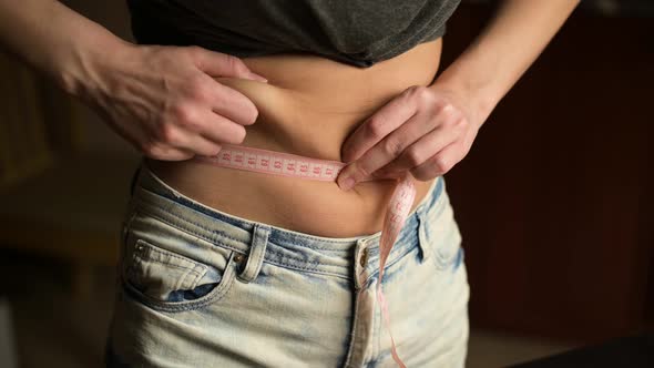 A young woman measures her obese belly next to a half-eaten pizza