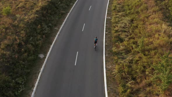 Aerial drone view of man cycling uphill along country road. 