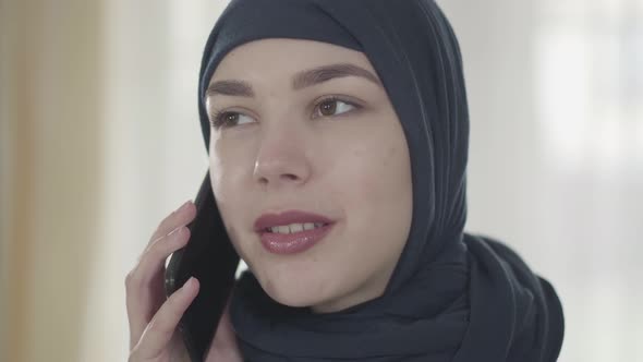 Portrait of a Young Beautiful Muslim Woman in Black Headdress Talking By Cell Phone Close Up. Cute