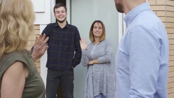 Happy Family Standing at Doors and Waving While Their Guests Leaving