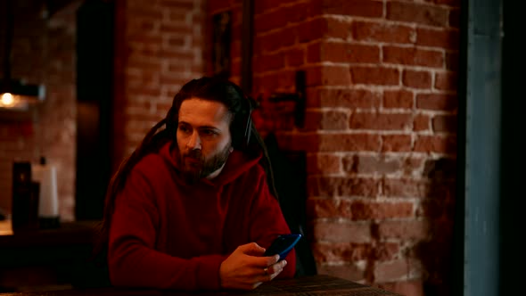 Handsome Young Man is Waiting Order in Cafe Listening Favorite Song By Smartphone and Headphones