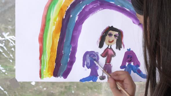 Little girl making rainbow and family on the window.