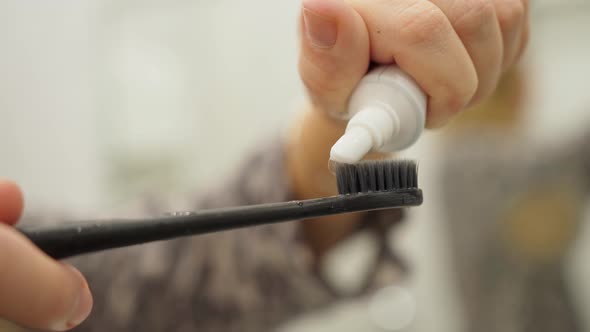 Female Hands Hold a Black Toothbrush and Squeeze White Toothpaste Onto It