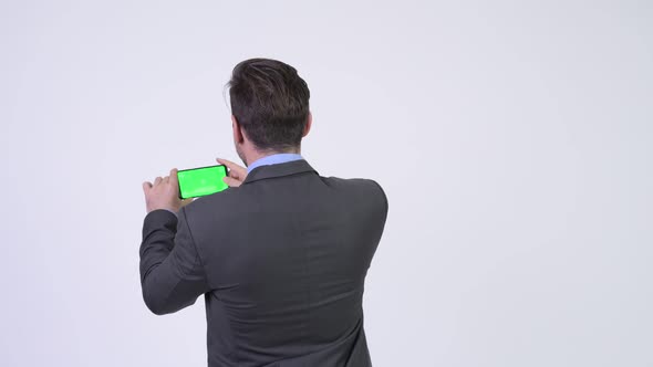 Rear View of Young Hispanic Businessman Taking Picture with Phone