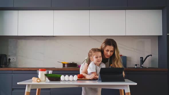 Mother and Little Daughter Stand in Kitchen