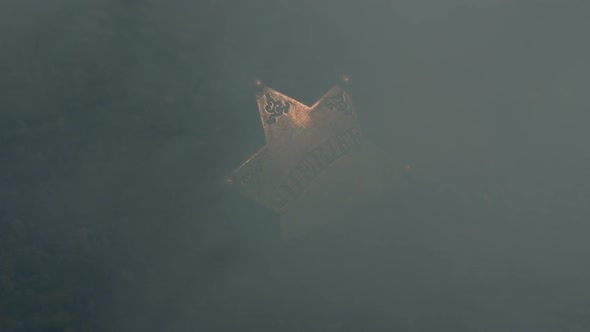 Sheriff Badge In The Ground With Smoke Blowing Over It