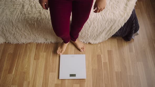 Woman in Burgundy Trousers Stands on a Floor Scale Barefoot to Measure the Weight