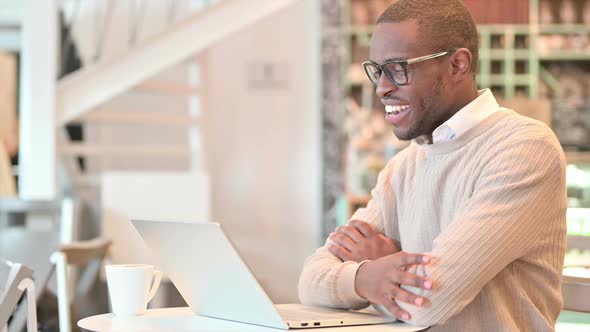 Cheerful African Man Talking on Video Call on Laptop in Cafe