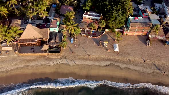 Aerial fly over shot of Sayulita main beach with waves crashing on the beach in Mexico during sunset