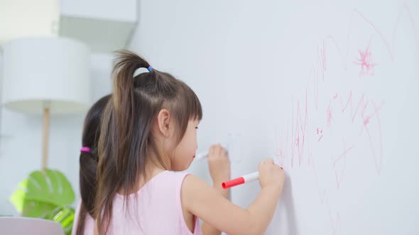 Asian young sibling kid girl enjoy paint on white wall in living room.