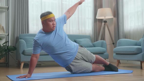 Fat Asian Man Doing Yoga In Side Plank Pose On Mat At Home