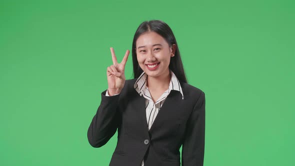 Asian Business Woman Showing Gesture Peace And Smiling While Standing On Green Screen In The Studio