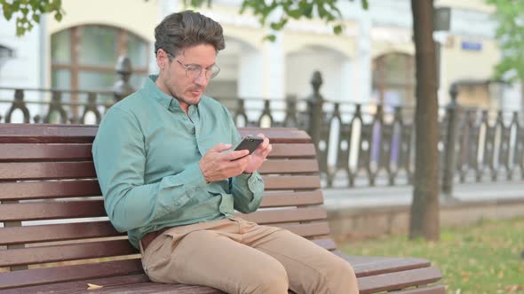 Man Browsing on Smartphone while Sitting on Bench