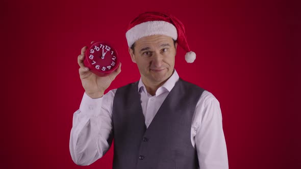 Cheerful Man in Santa Hat Pointing at Clock Reminds Minutes Before New Year Eve