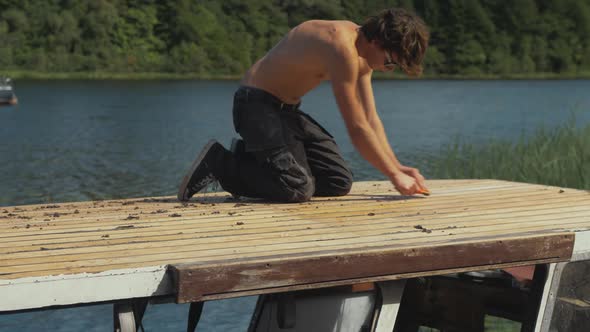 Young male carpenter using sharp scraper planing wooden roof planking of timber boat by hand. WIDE S