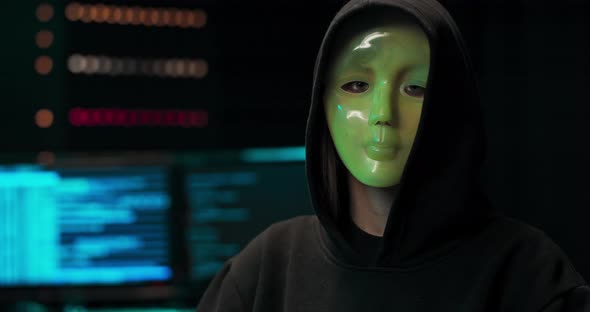 Closeup Shot of a Masked Hacker in a Hoodie Sitting in the Middle of Data