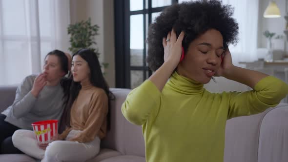 Young Attractive African American Woman Enjoying Music in Headphones Dancing Sitting on Couch