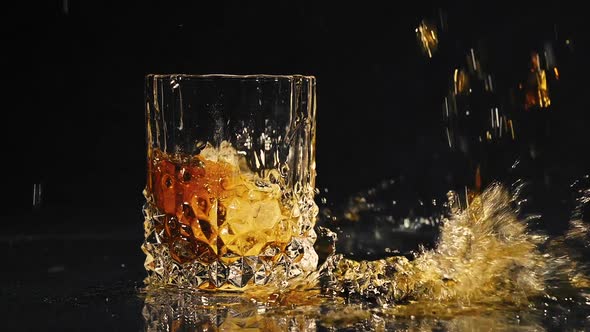 Ice Dropped Into Glass of Whisky Splashing in Slow Motion. 