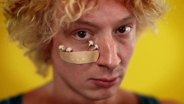 Closeup Male Queer Person Face with White Flowers Attached with Medical Patch