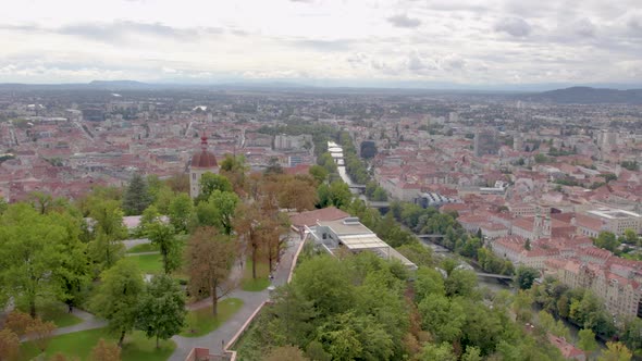 Wide aerial orbit view flying around landmark Glokenturm tower on Graz's Schloßberg hilltop woodland