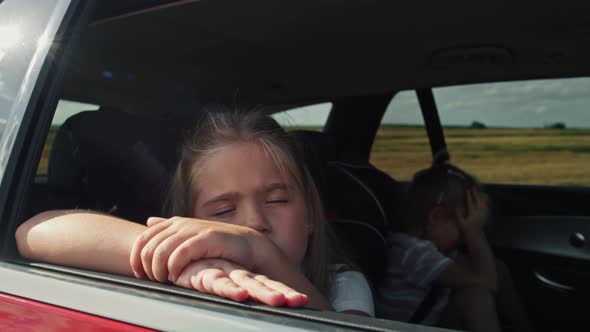 Caucasian girl of 8 years looking out of the car window while car trip and her sister in the backgro