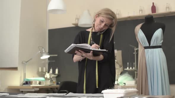 Blonde Caucasian Female in Black Dress with Tailor's Meter Around Neck Talking on Mobile Phone