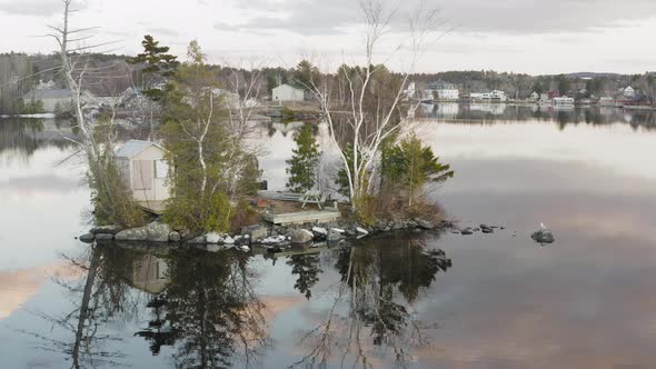 Tiny sparse island with a small shack on a calm lake at dusk AERIAL SLIDE