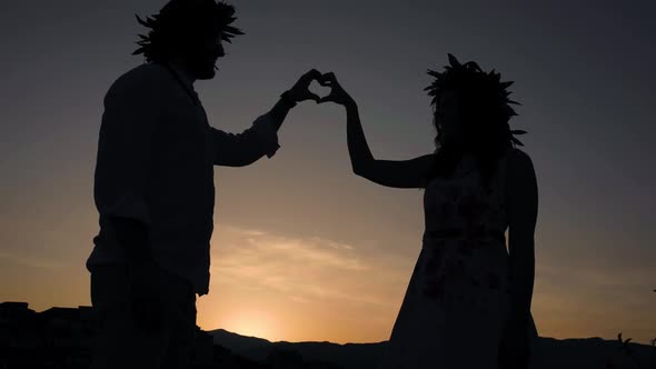 Silhouette of of a couple making the heart symbol with graduation crowns