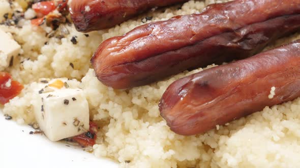 Fried sausages and cous-cous served on plate close-up 4K 2160p 30fps UltraHD tilting footage - Steam