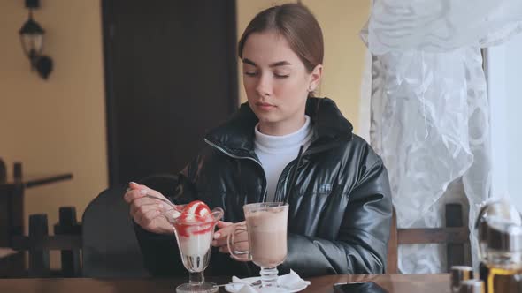 A Girl is Eating Ice Cream in Front of a Cappuccino in a Coffee Shop