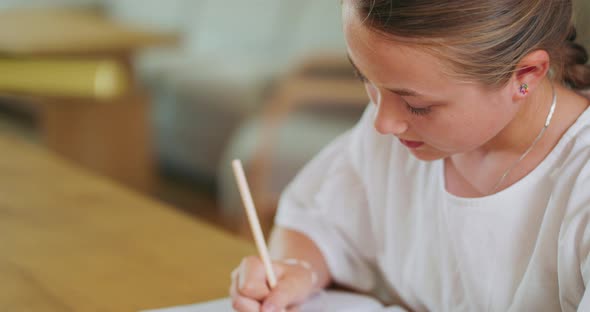 Closed Focused Teen Girl at the Desk Does Tasks in Workbook and Checks Them on Laptop Background is alt