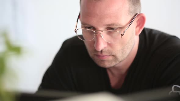 Man Works in an Office at a Computer. His Eyes Are Tired and He Takes Off His Glasses. Close Up.