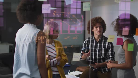 Diverse work colleagues writing and drawing on glass wall having a discussion