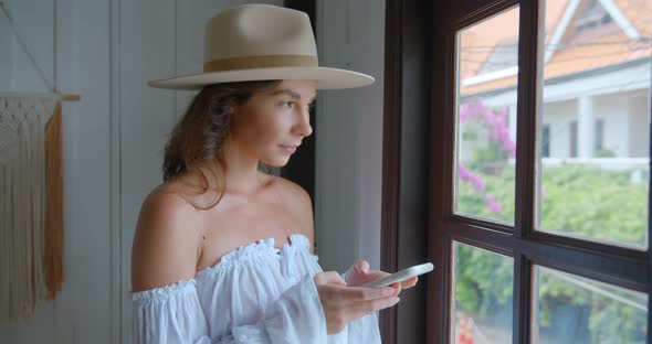 Woman Stands By the Window and Typing the Massage She Looks to the Window and Smiles