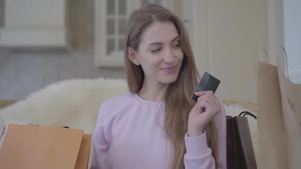 Portrait of a Confident Smiling Young Cute Girl Sitting on the Sofa with a Lot of Shopping Bags