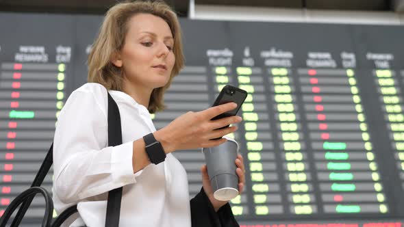 Woman At International Airport Checking Flight Information On Phone Application