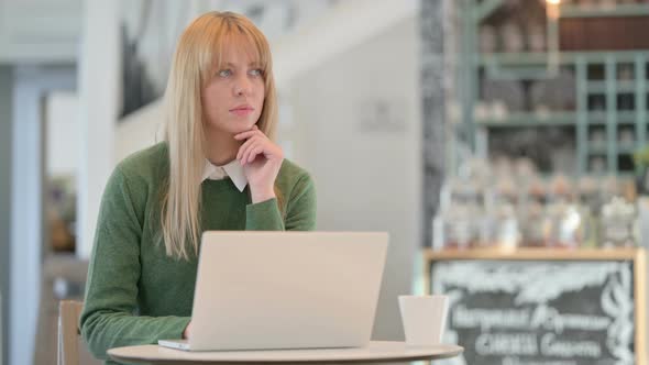 Young Woman Thinking While Using Laptop in Cafe