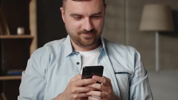 Happy Young 30s Man Looking at Smartphone Screen Reading Message with Pleasant News Enjoying