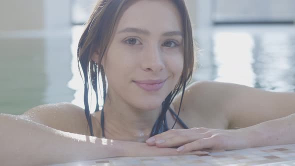 Close-up Face of Charming Brunette Woman Posing at Poolside and Smiling at Camera. Portrait of