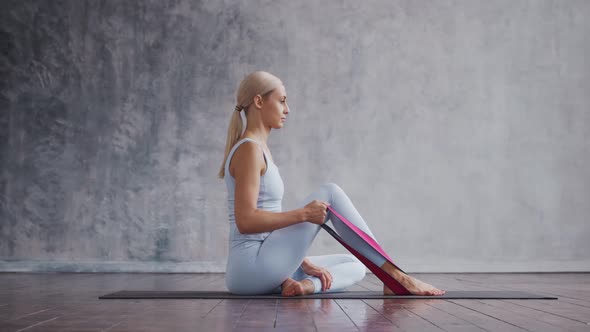 Young and sporty girl in sportswear is doing exercises in home interior using resistance band.