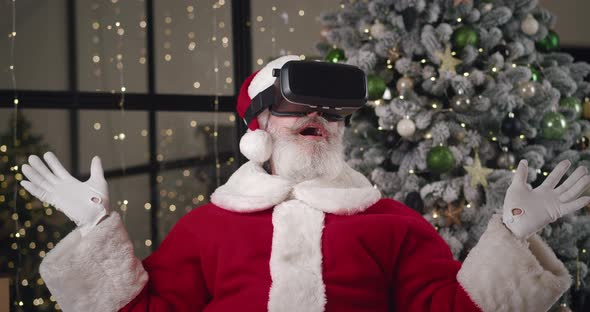 Curious Elderly Charming Caucasian Man in Santa Claus Carnival Costume Puts on VR Glasses and