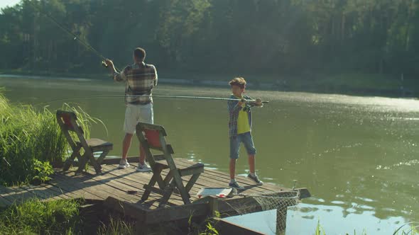 Positive African American Father and Son Fishing Together on Pond at Sunrise