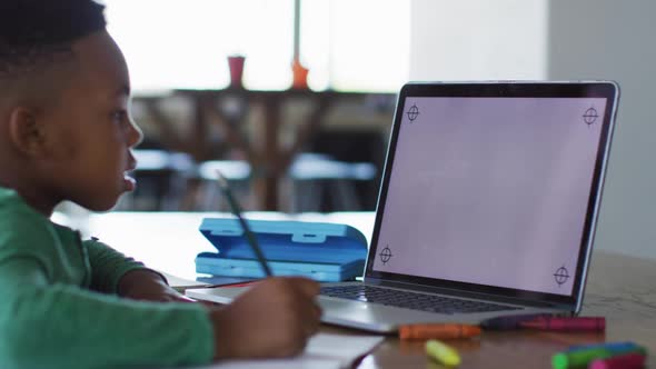 African american boy having a video call on laptop with copy space while doing homework at home