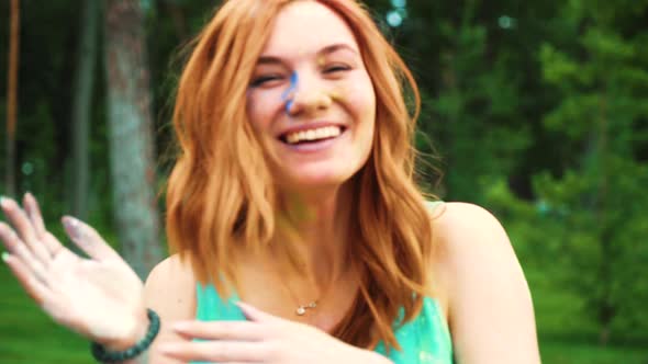 red haired young woman smeary with colorful powder after Holi laughing at camera