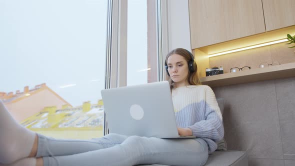 Woman works at home at a laptop near the window, it is snowing outside the window. Remote work.