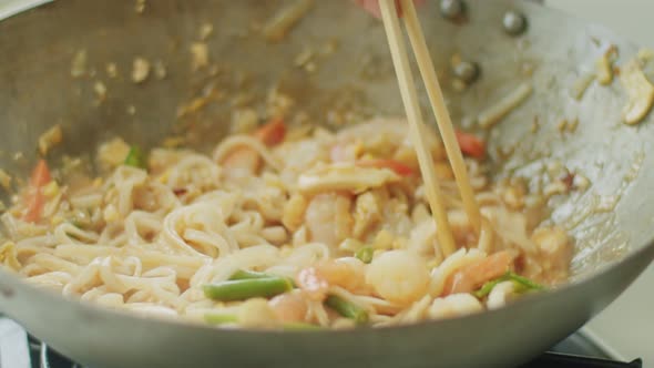 Woman stirring hot wok noodles with chopsticks